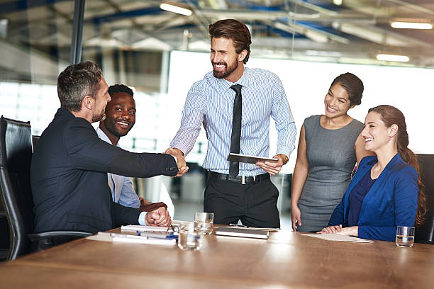 Shot of two colleagues shaking hands while in a meeting with colleagues in a boardroom